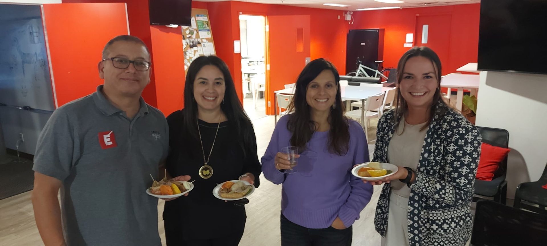 Quatre personnes tenant des assiettes de nourriture dans une pièce aux murs orange.