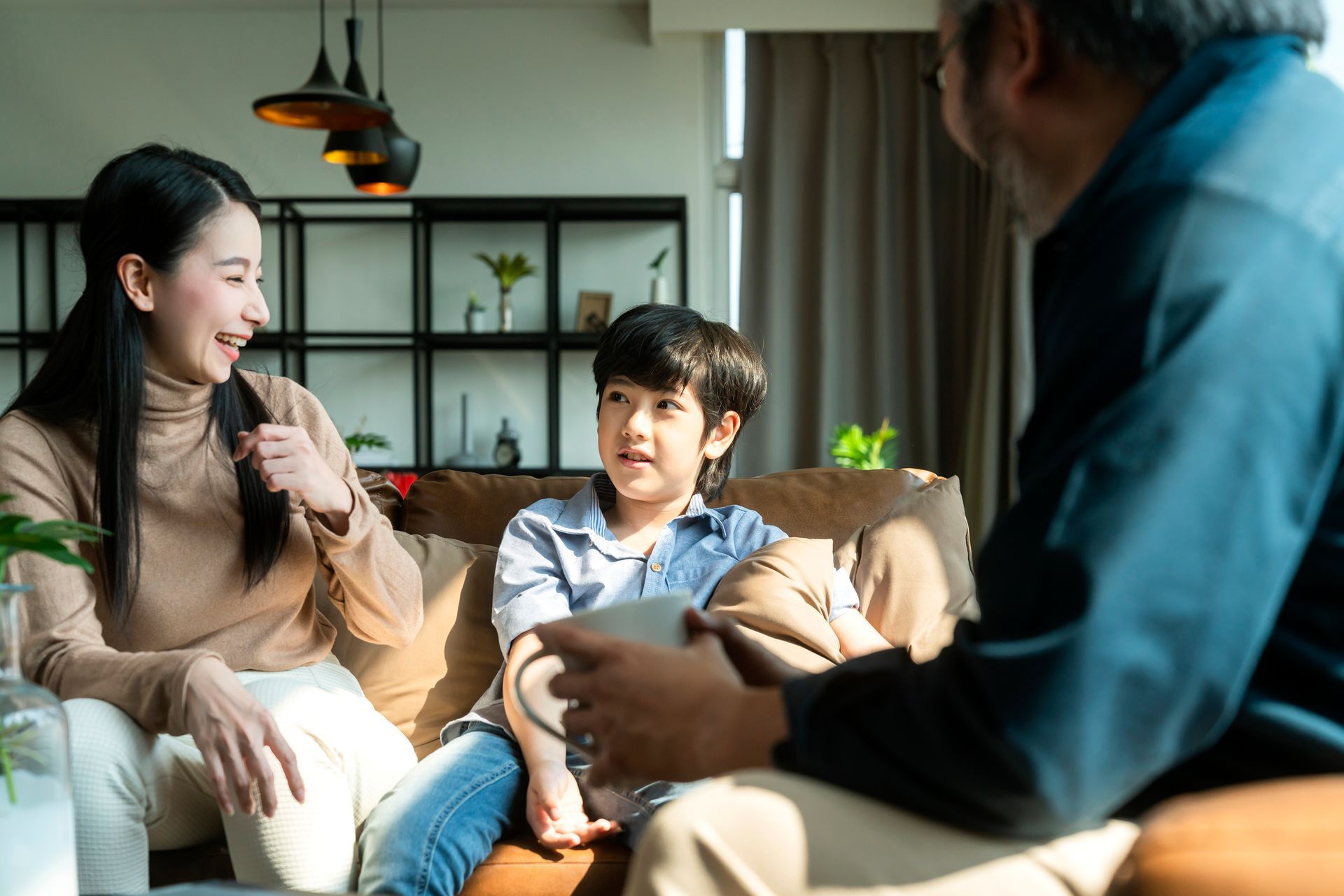 A family of three smiling on a couch in a living room, talking together.