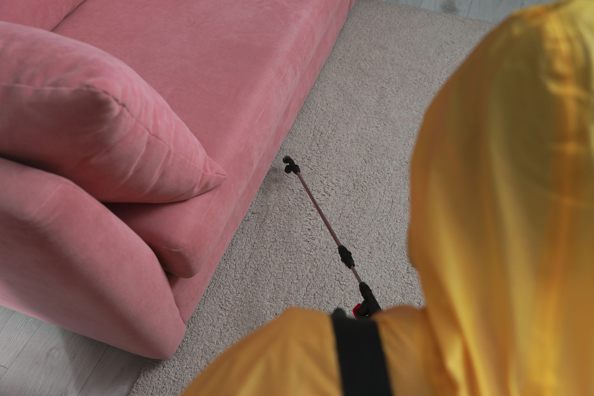Person in Yellow Suit Spraying Near Pink Couch — Rohan's Maintenance in Robina, QLD