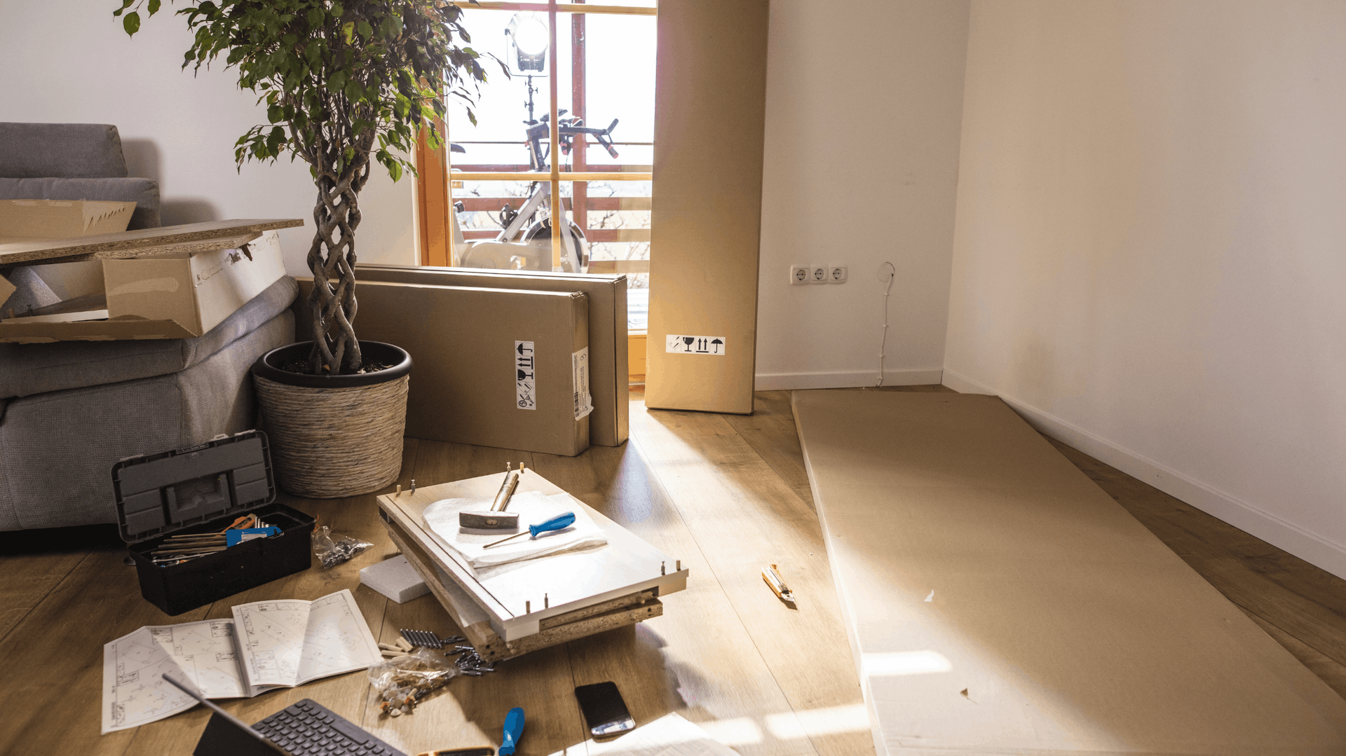 Room with disassembled furniture, tools, and instructions. Cardboard boxes and wood planks on the floor — Rohan's Maintenance in Robina, QLD