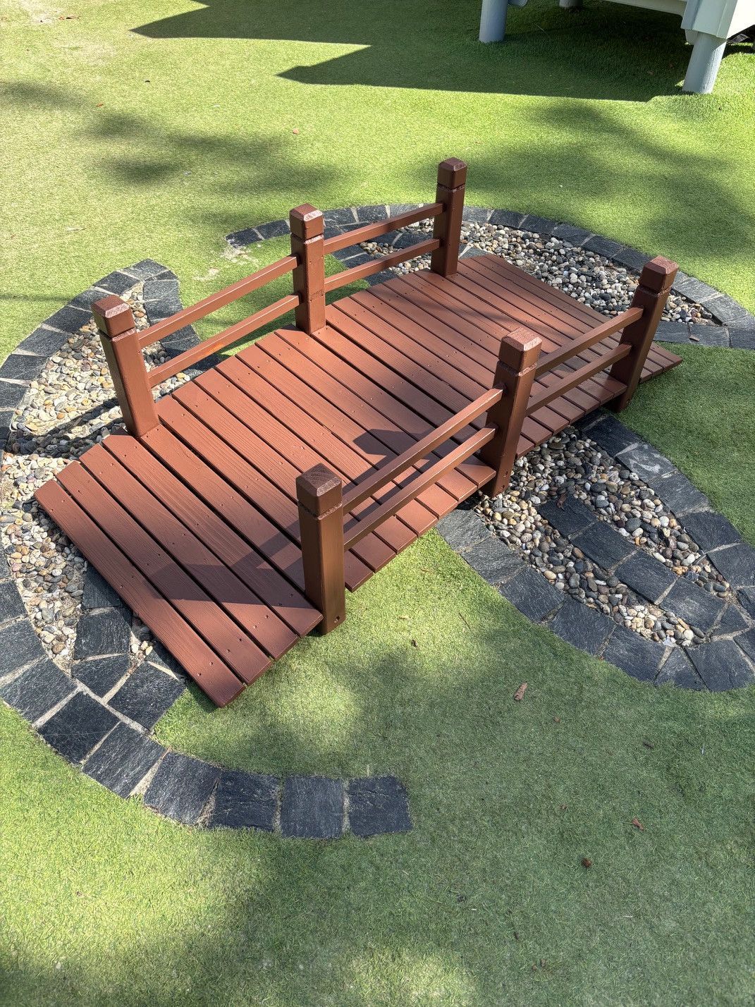 Wooden bridge in a garden, crossing a gravel bed surrounded by green turf — Rohan's Maintenance in Robina, QLD