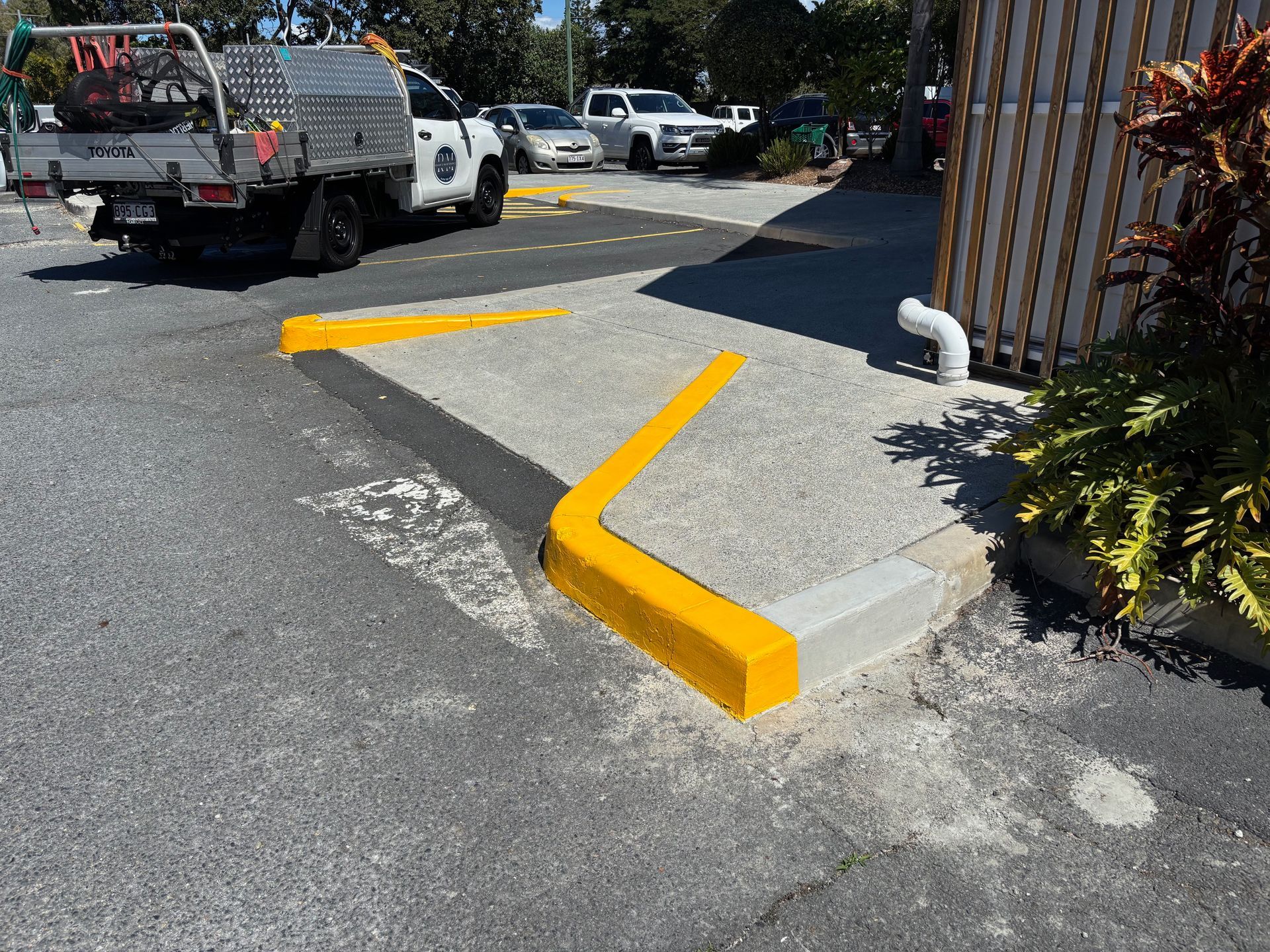 Yellow painted curb at a parking area entrance, next to a building and work truck — Rohan's Maintenance in Robina, QLD