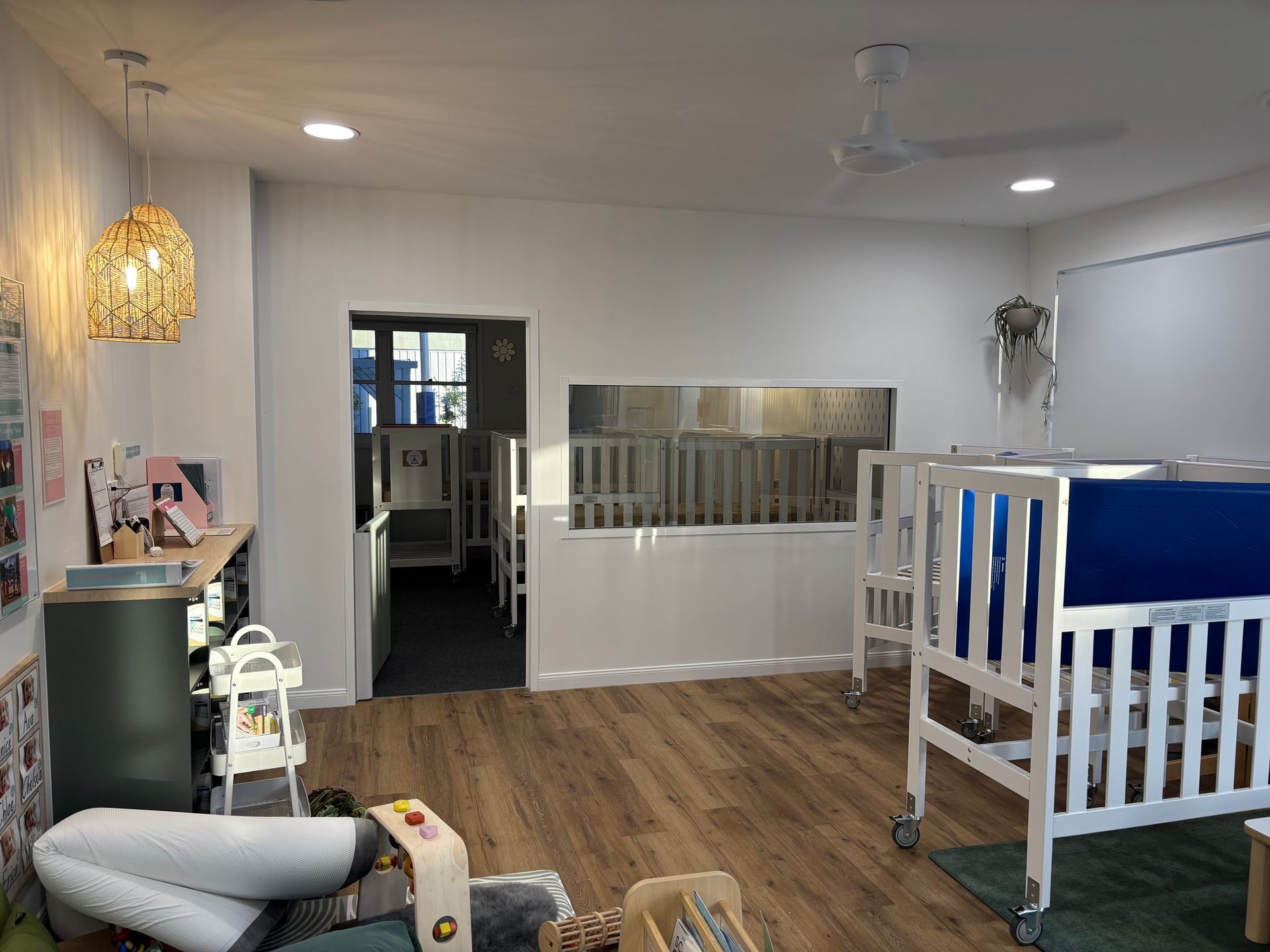 Daycare room with cribs behind glass, beanbags, and plants. Wooden floor, white walls, and disco ball — Rohan's Maintenance in Robina, QLD
