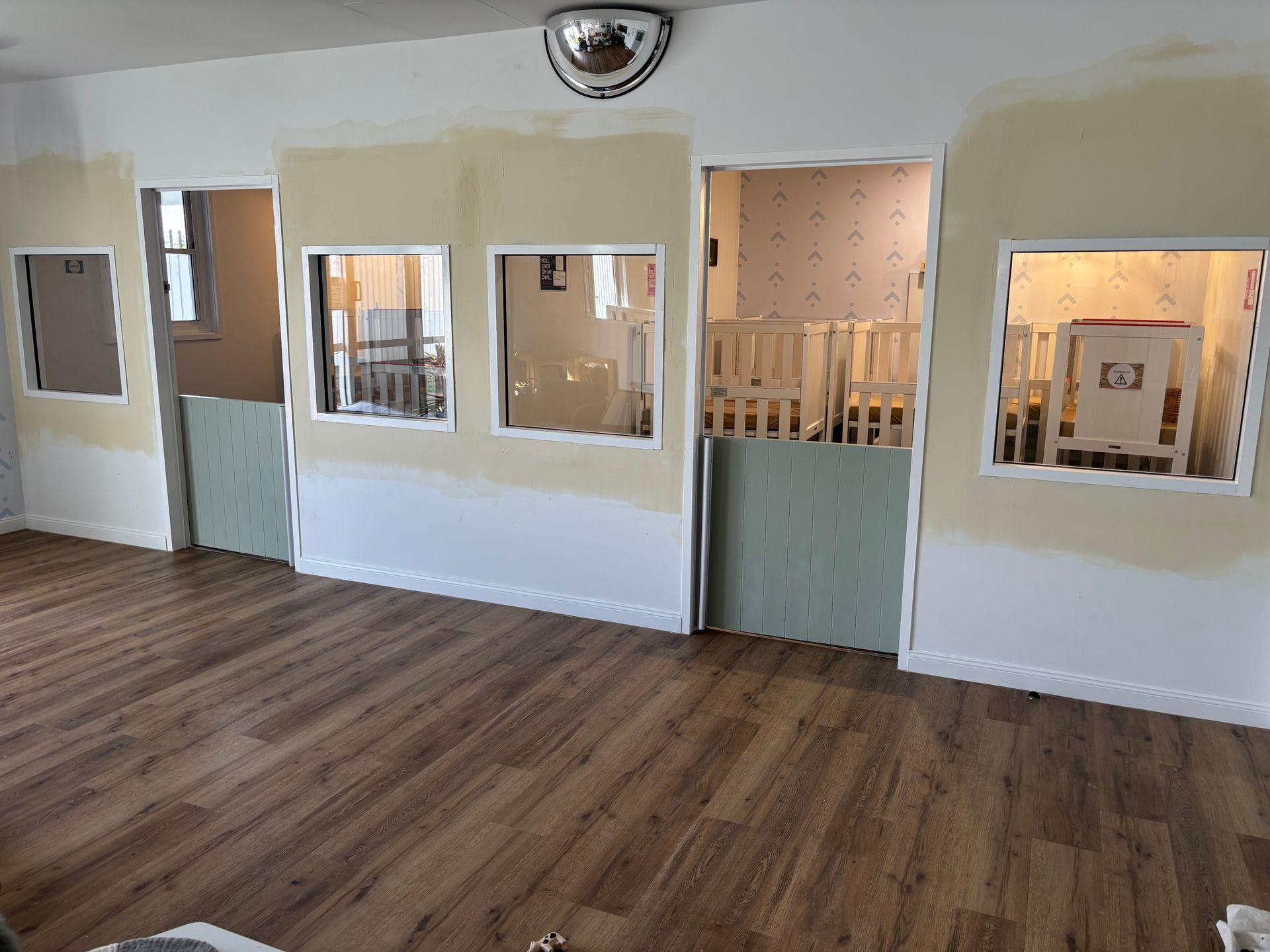 Nursery room with cribs, wooden floors, and a vacuum cleaner. A window and door are visible — Rohan's Maintenance in Robina, QLD