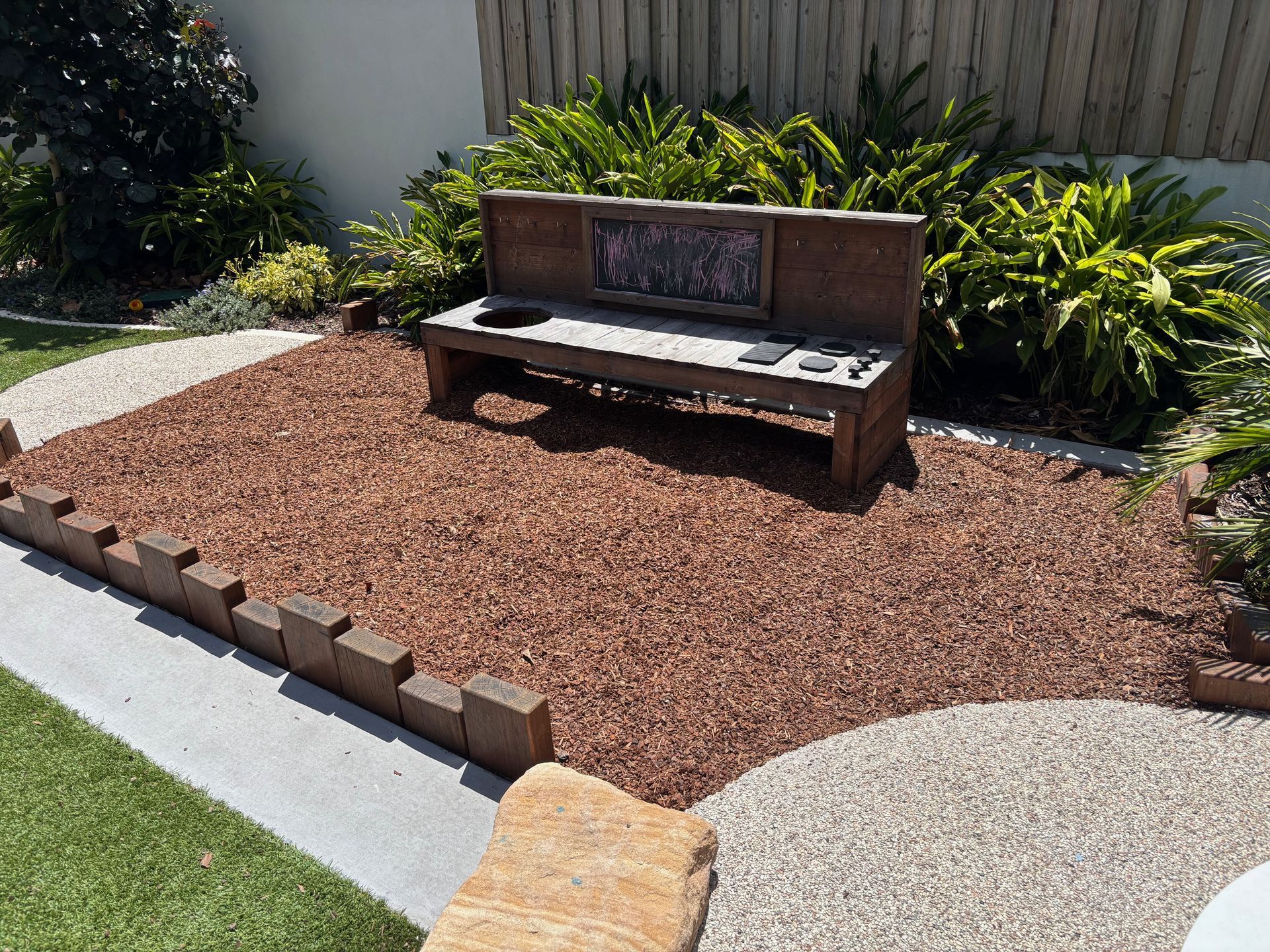 Wooden deck overlooking a gravel pathway leading to a green garden with lush plants — Rohan's Maintenance in Robina, QLD