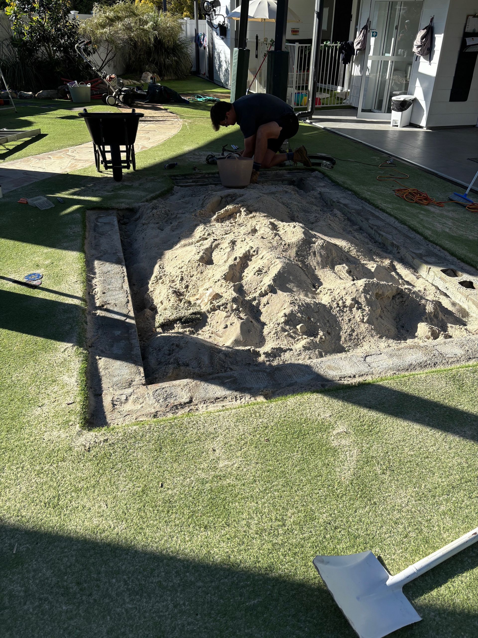 Person filling a sandbox with sand in a backyard on a sunny day — Rohan's Maintenance in Robina, QLD