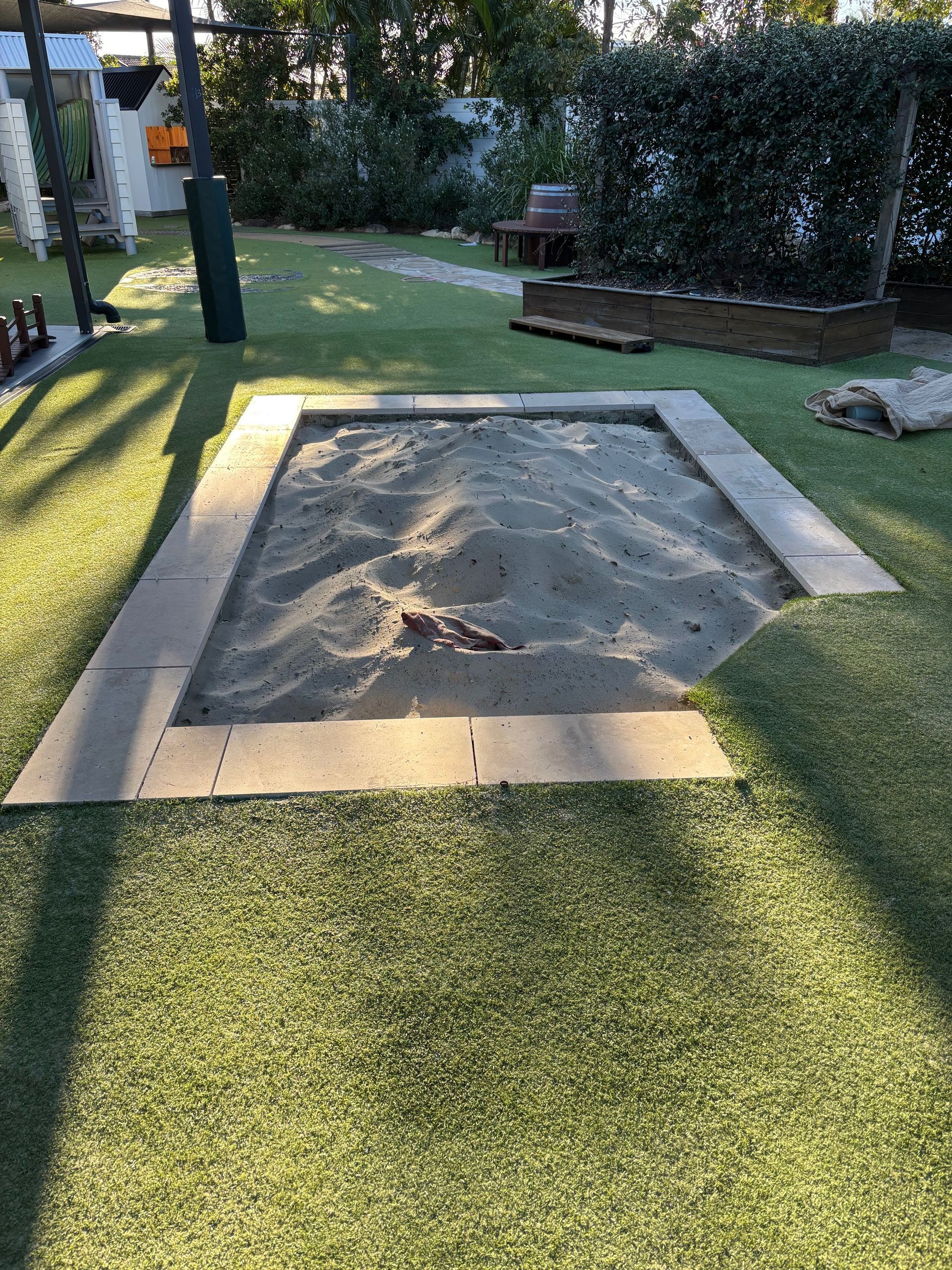 Sandbox in a grassy play area, bordered by gray paving stones — Rohan's Maintenance in Robina, QLD