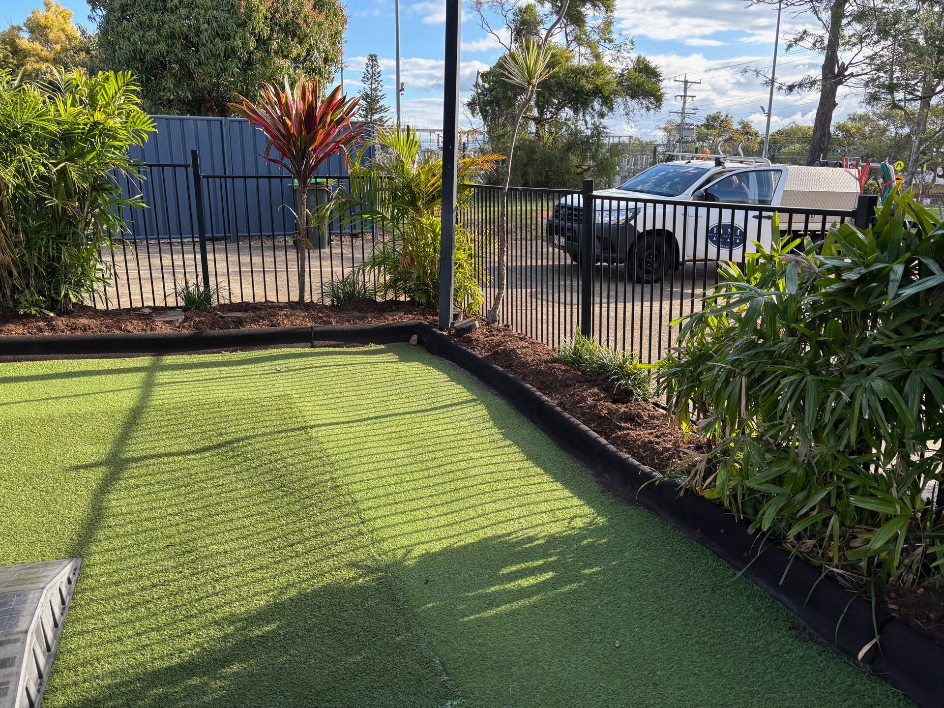 Green artificial grass in foreground with green shrub and rock border in the background — Rohan's Maintenance in Robina, QLD
