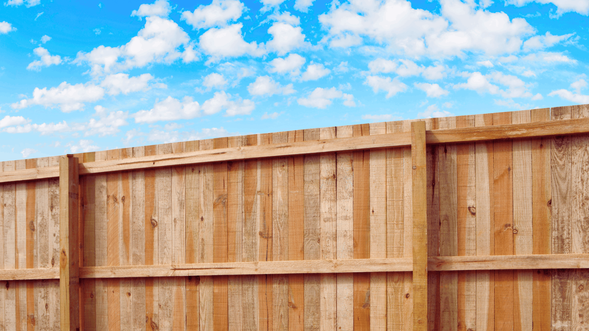Wooden fence against a blue sky with fluffy white clouds — Rohan's Maintenance in Robina, QLD