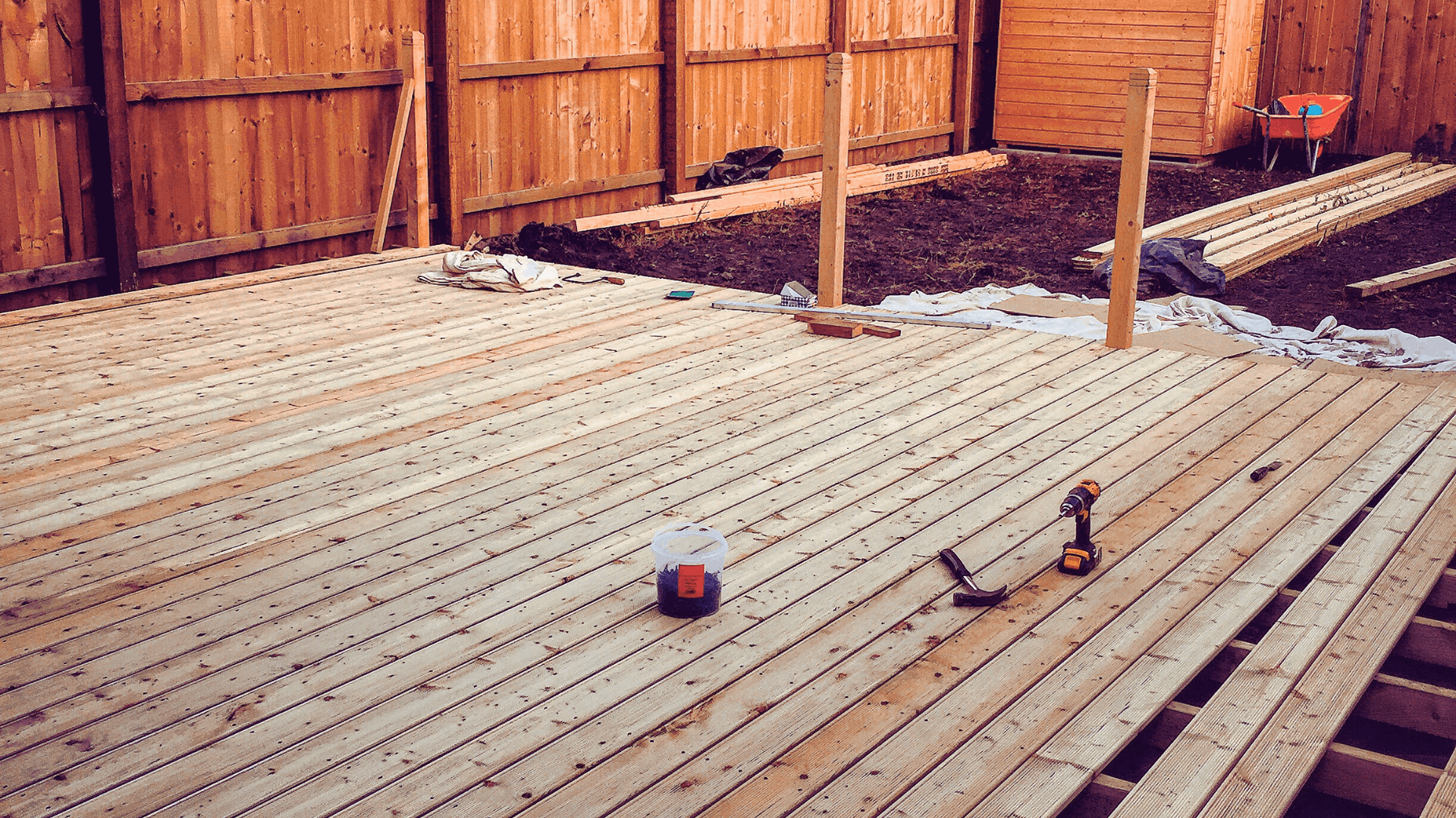 Wooden deck under construction in a backyard, brown fence in the background, tools and materials scattered — Rohan's Maintenance in Robina, QLD