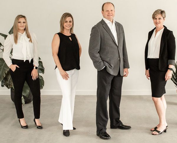 Four professionals stand side-by-side in a bright, neutral office space, posing for a group portrait.