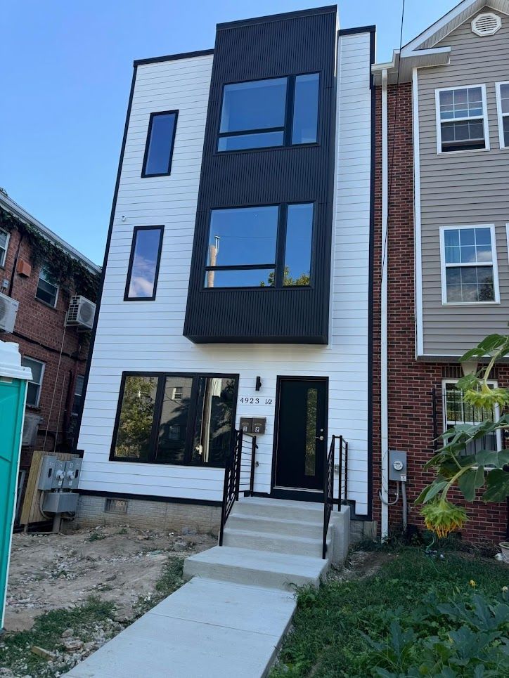 Bright kitchen with white cabinets, island with brown barstools, and black-framed windows.
