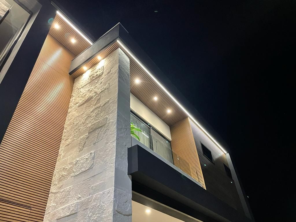 Modern building exterior with stone facade and wood paneling, lit by nighttime lights.