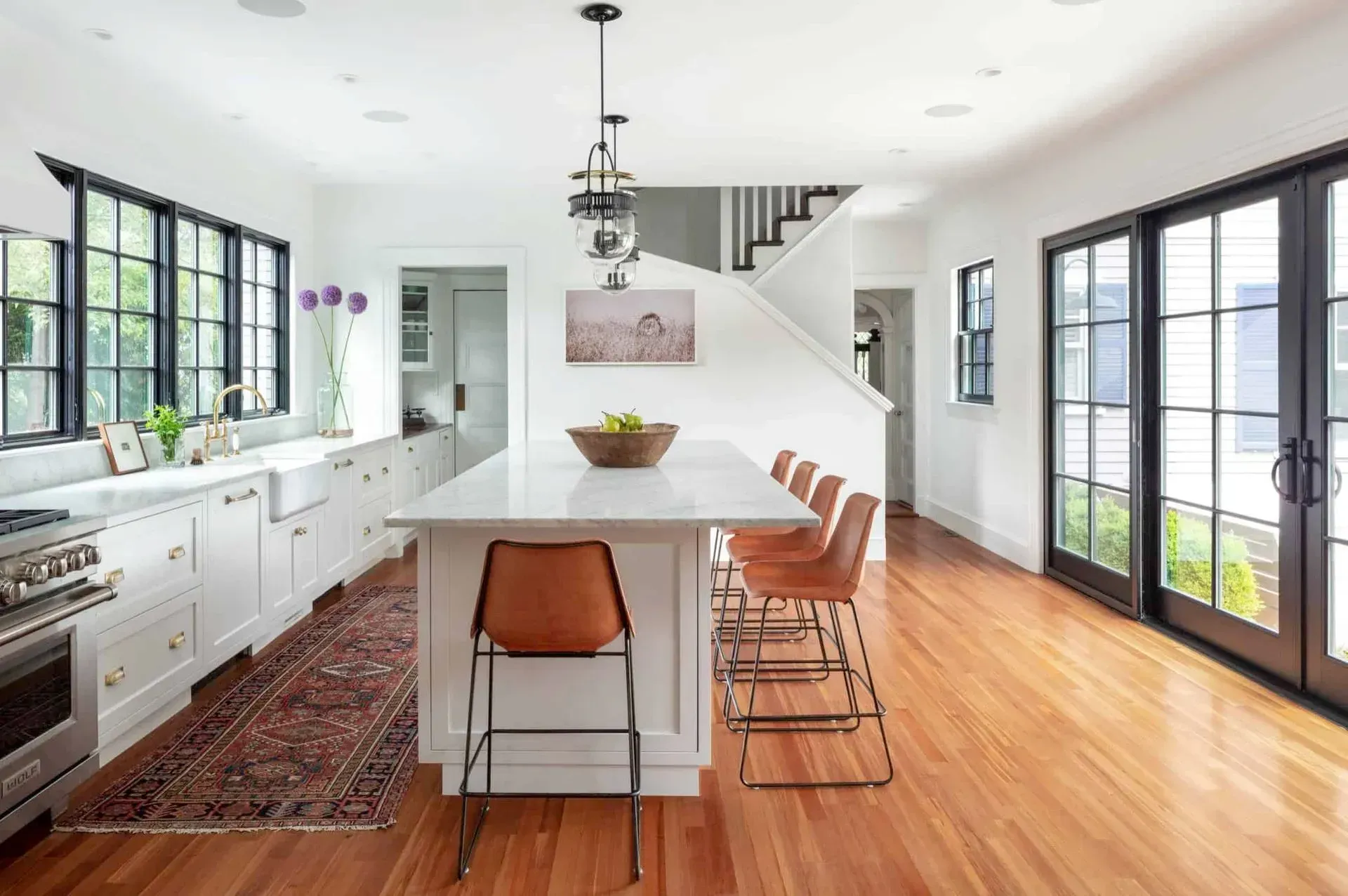 Bright kitchen with white cabinets, island with brown barstools, and black-framed windows.
