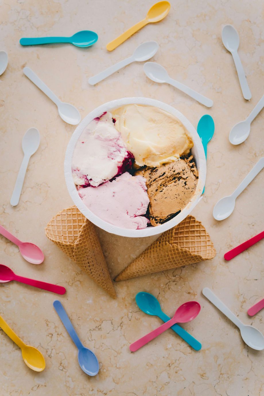 Ice cream in a waffle cone bowl with colorful plastic spoons scattered around it