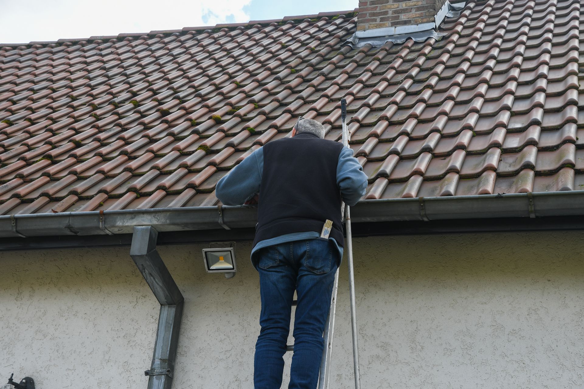 Professional roofer cleaning residential gutter while balancing on metal ladder.