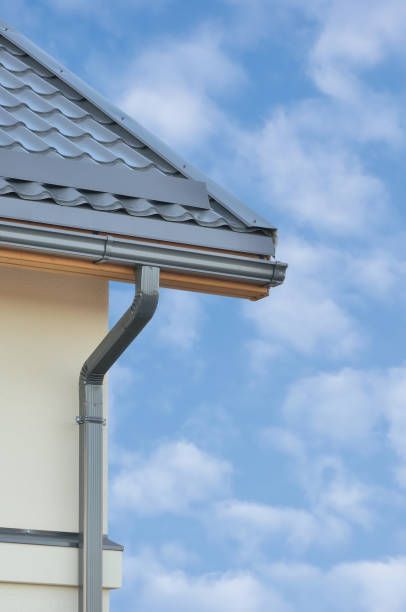 Gray roof and gutter on a cream-colored building against a blue, cloudy sky.