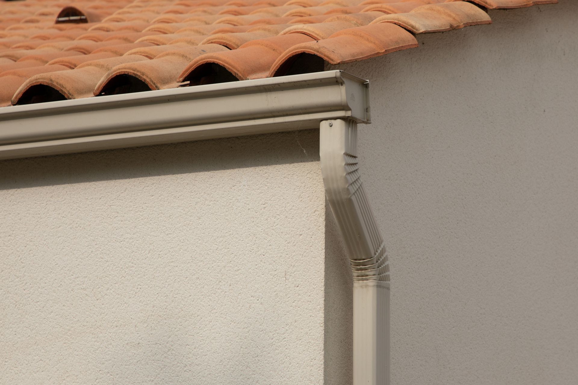 Seamless rain gutter installed on a modern sandy beige home corner roof.