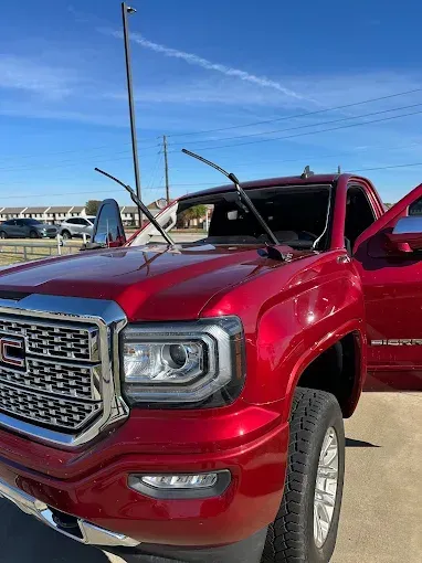 Red GMC truck with shattered windshield and open door on a sunny day.