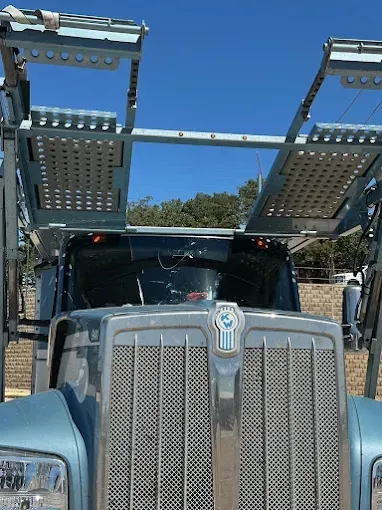 Blue Kenworth car carrier truck under a clear blue sky.