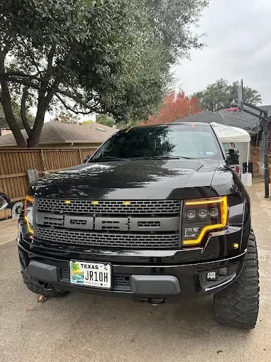 Black Ford Raptor truck with yellow headlights and Texas license plate parked outdoors.