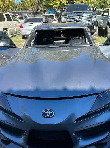 Gray Toyota Supra with broken windshield, parked outside.