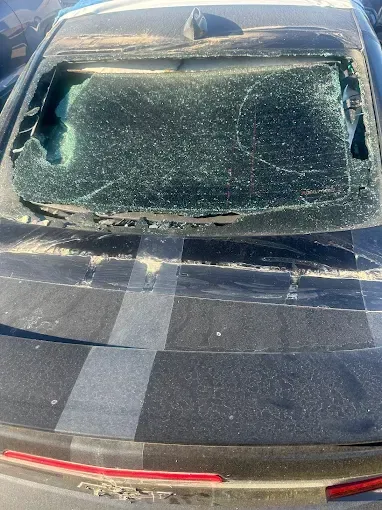 Black car rear with shattered glass. A red tail light and black and gray stripes are visible.