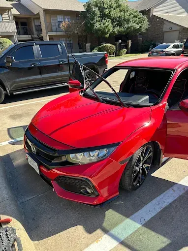 Red Honda Civic parked outdoors with door open, black truck and other cars in the background.