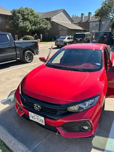 Red Honda Civic parked in front of an apartment building; door open. Black truck on the left. Texas license plate.
