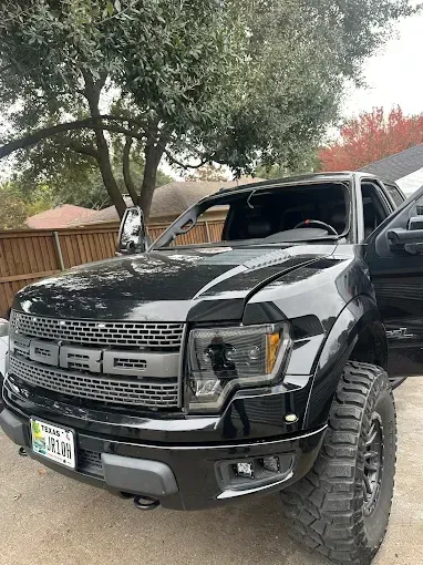 Black Ford Raptor truck with the door open, in front of a tree.