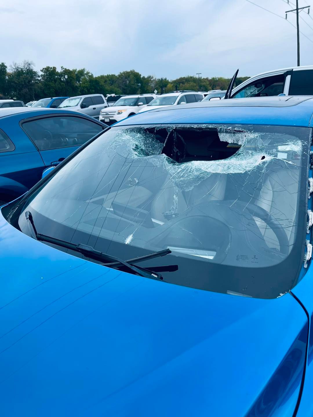 Blue car with a shattered windshield in a parking lot.