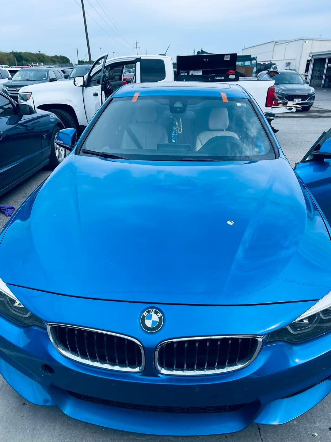 Blue BMW car with orange tape on the windshield, in a parking lot.