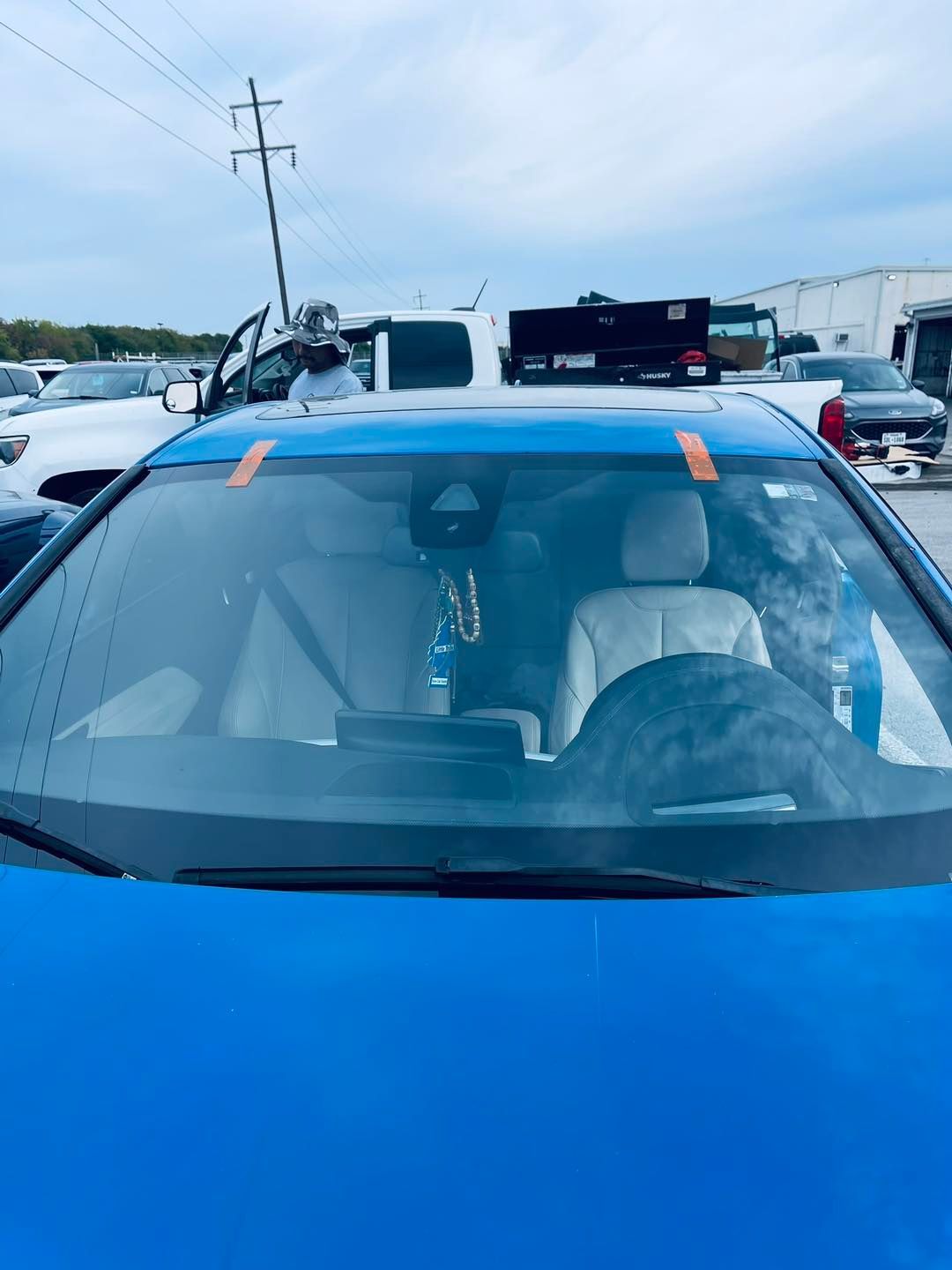 Blue car with new windshield. A person outside is working on it.