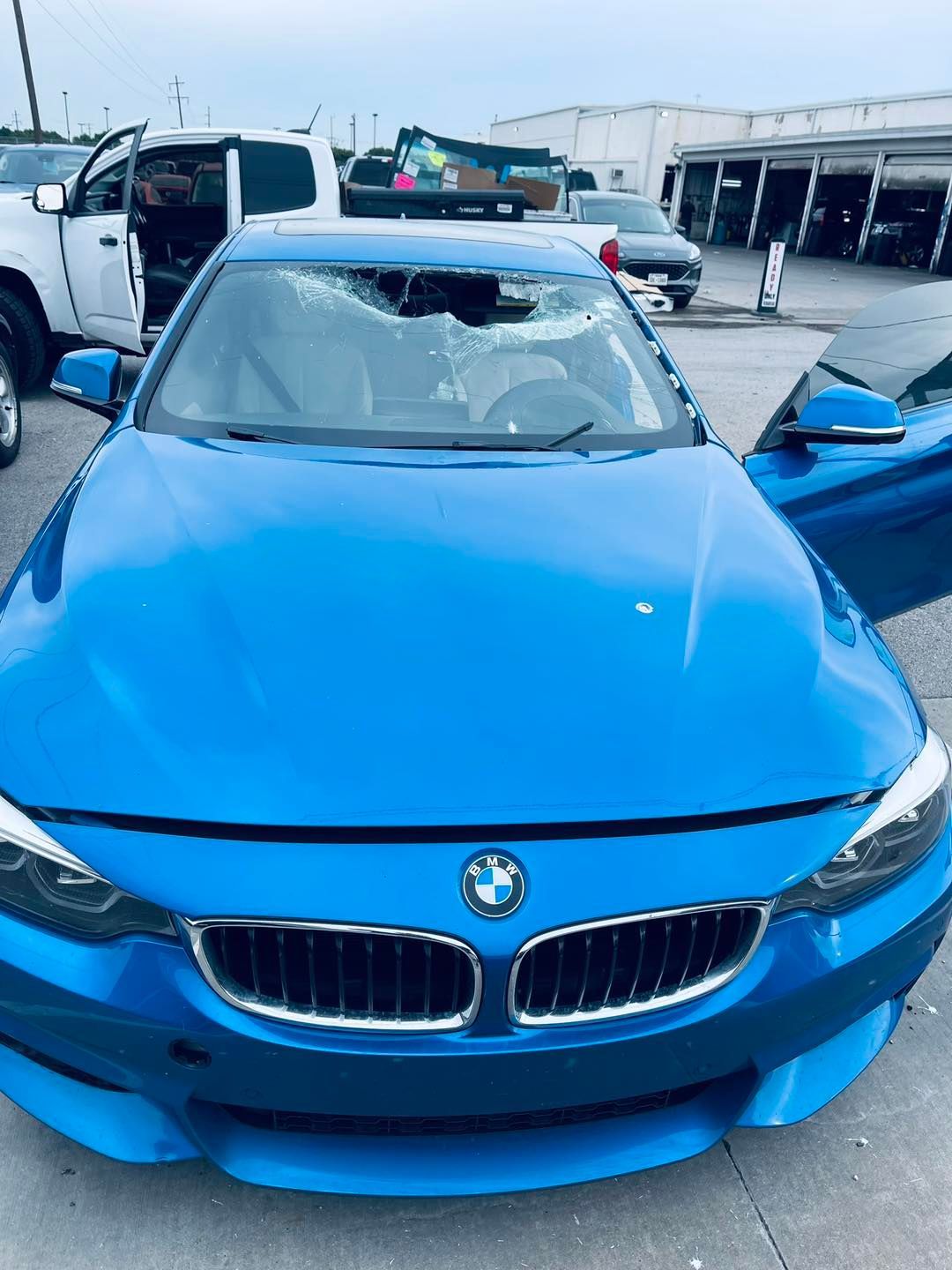 Blue BMW with smashed windshield and open doors parked outside.