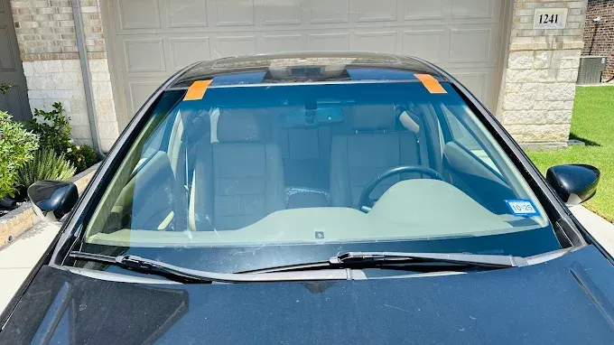 Black car with orange tape on windshield, parked in front of a garage.