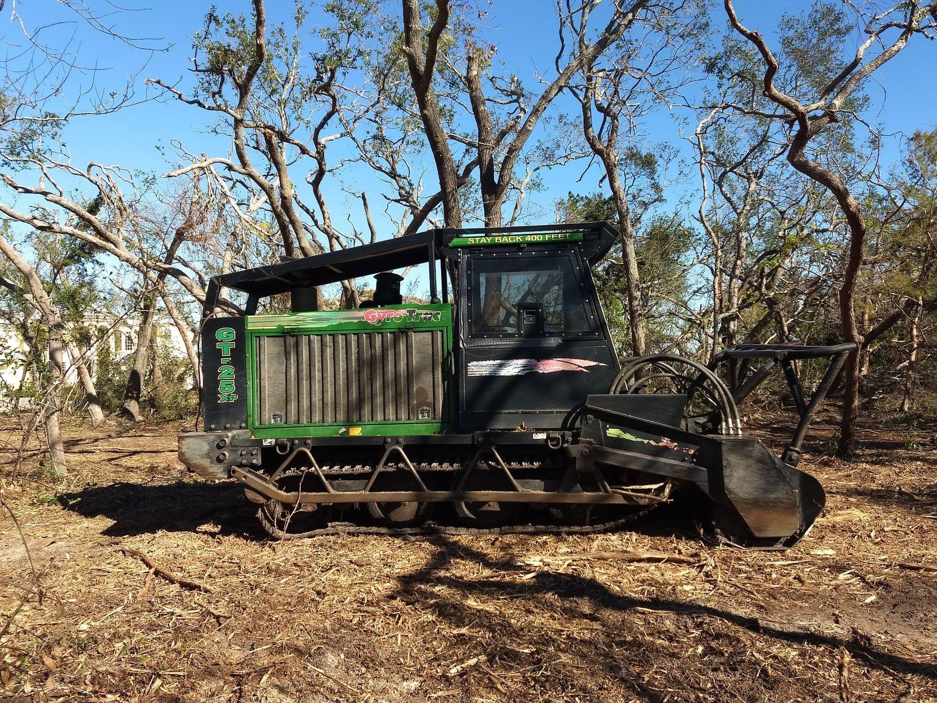 A green and black tractor is parked in a field with trees in the background.