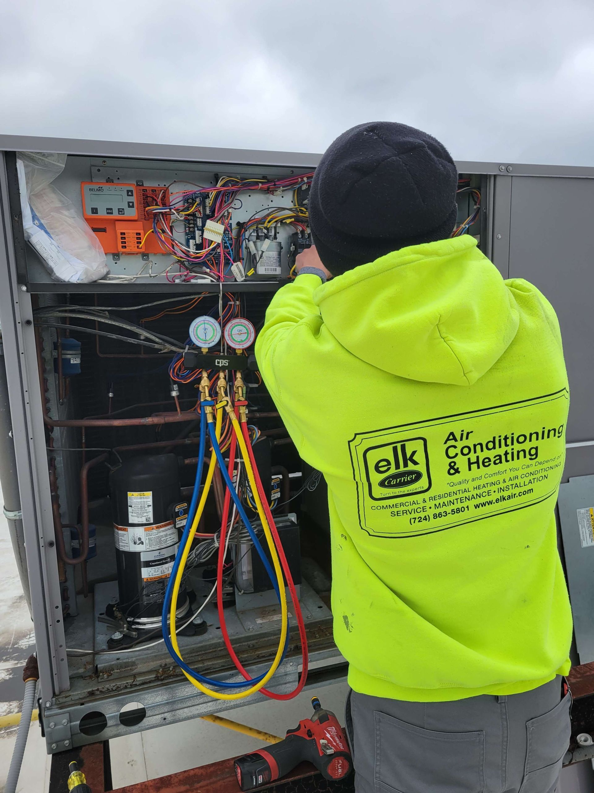 A man in a neon yellow hoodie is working on an air conditioner.