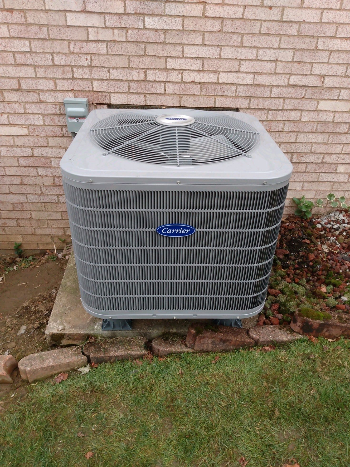 A carrier air conditioner is sitting outside of a brick building.