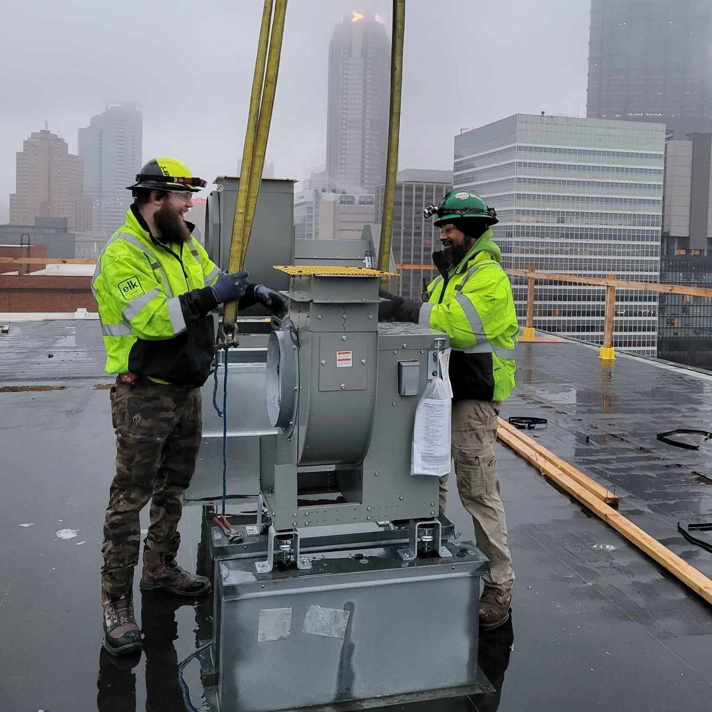 Two men are working on a fan on top of a building