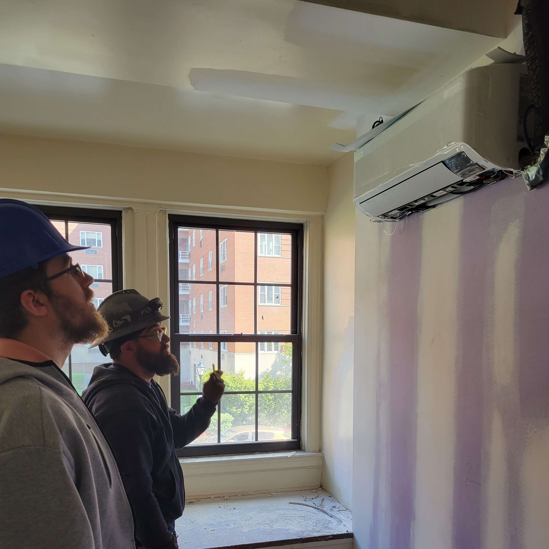 Two men are standing in a room looking out a window.