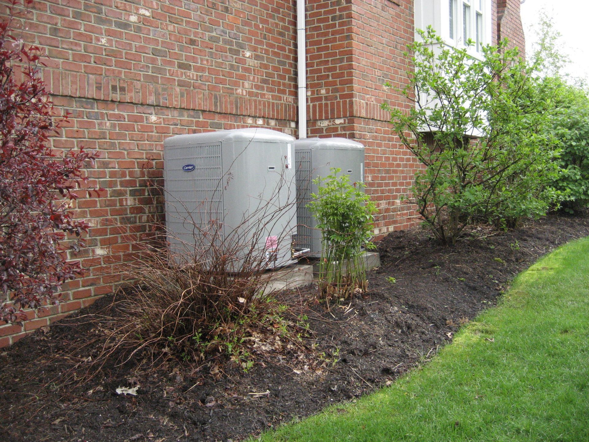 Two air conditioners are sitting on the side of a brick building.