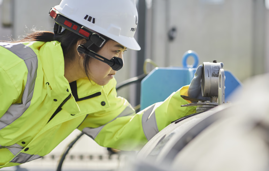 A woman wearing a hard hat and safety vest is working on a machine.