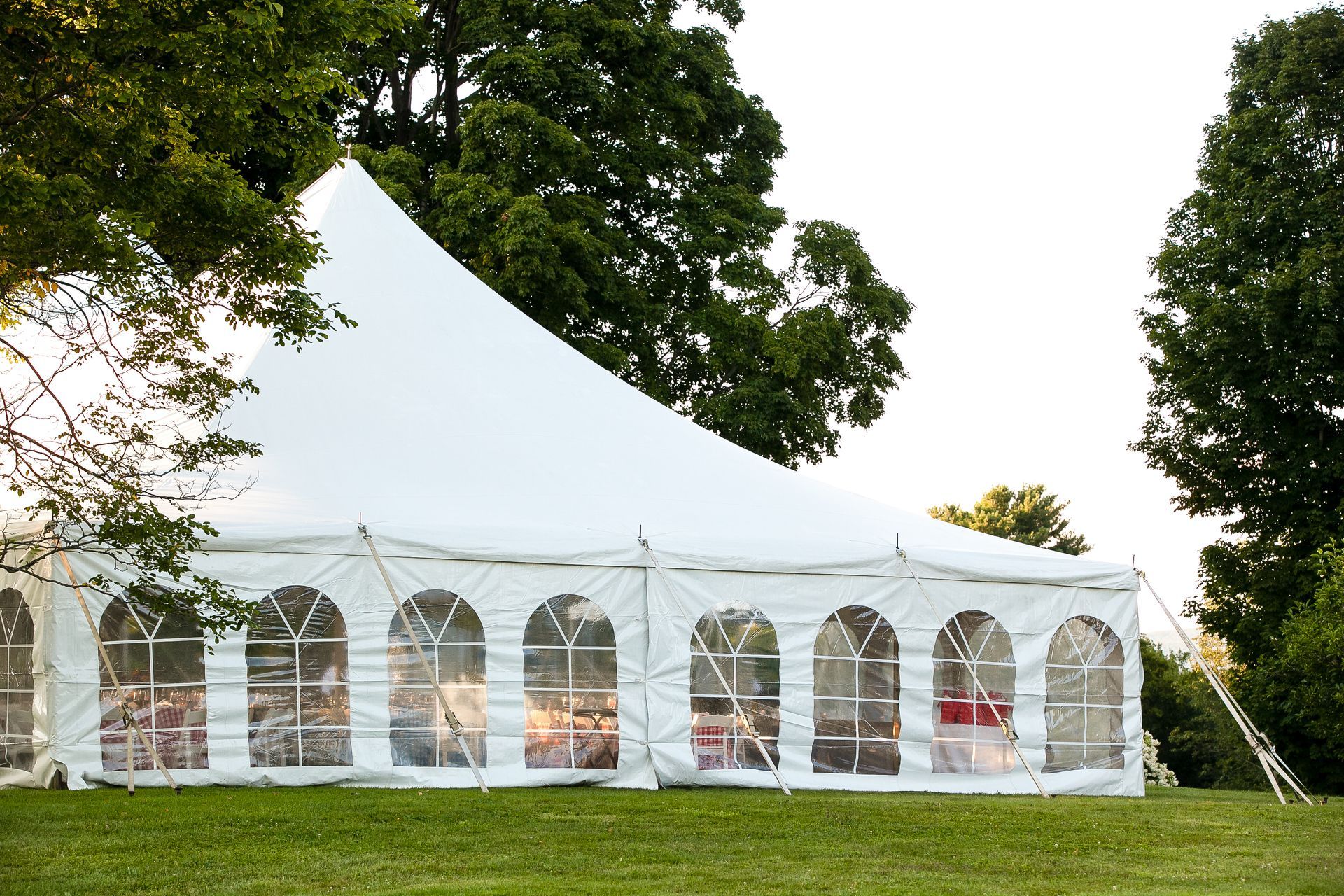 White tent with arched windows on a grassy lawn, trees in the background