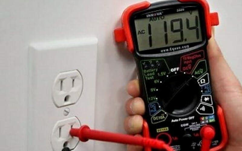 A person is using a digital multimeter to test an electrical outlet.