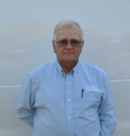 A man in a blue shirt and sunglasses is standing in front of a white wall.