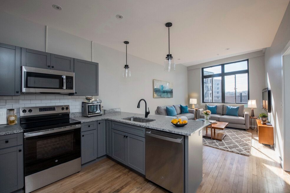 A kitchen with gray cabinets , stainless steel appliances , a microwave and a sink.