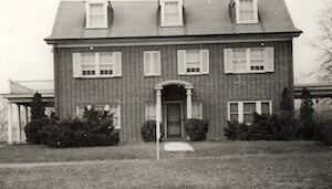A black and white photo of a large brick house with shutters on the windows.
