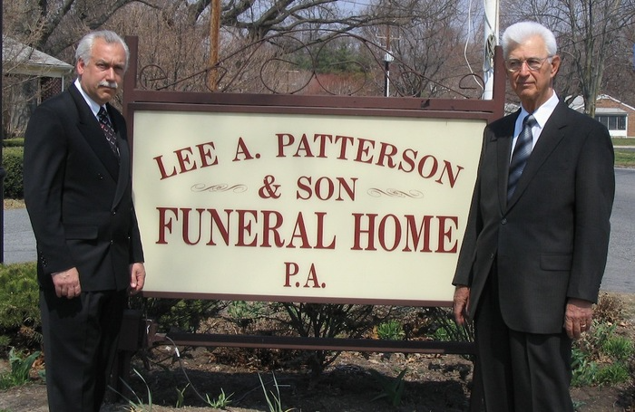 Two men standing in front of a sign for lee a. patterson & son funeral home pa