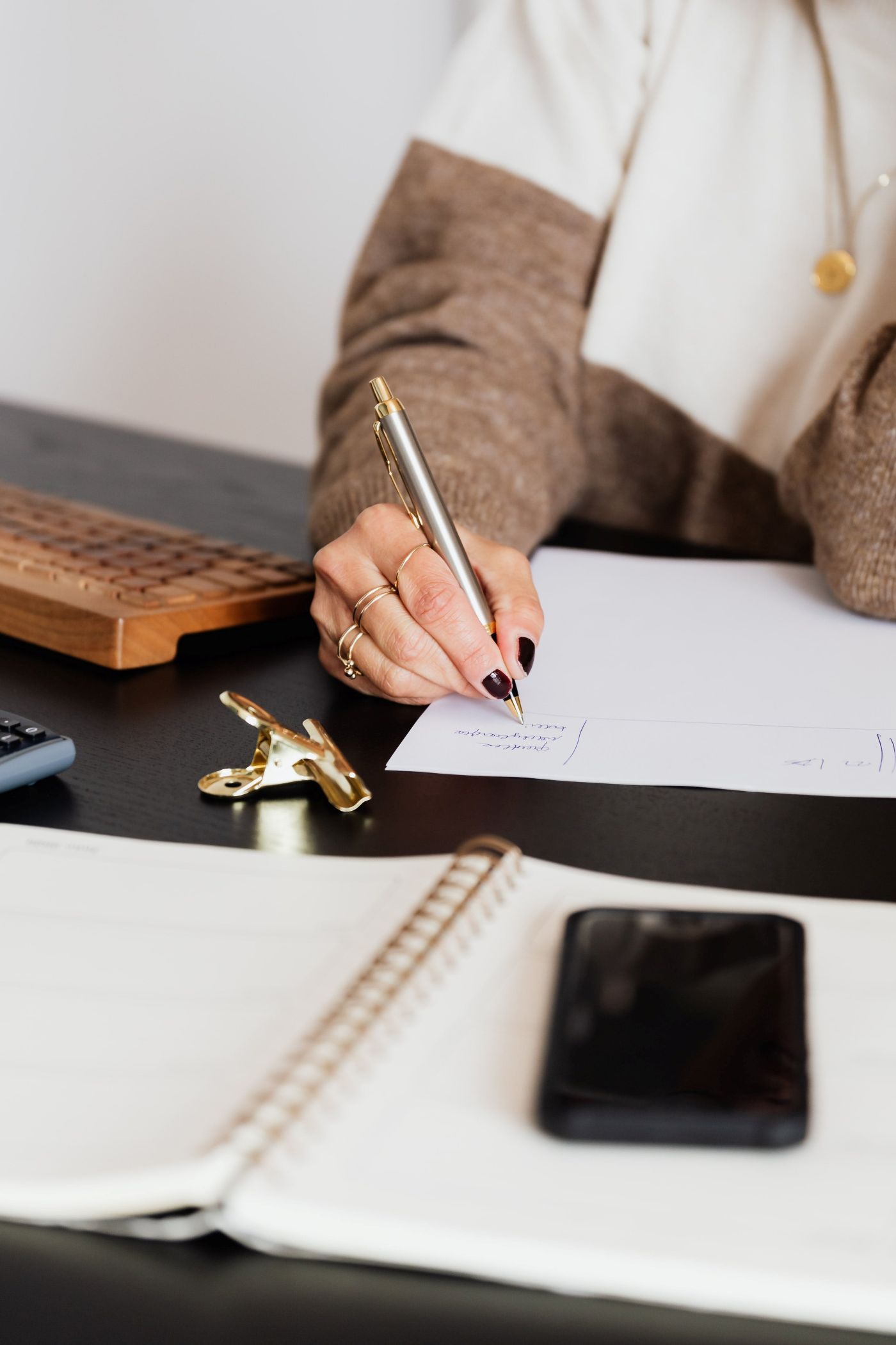 A woman is sitting at a desk writing in a notebook with a pen.