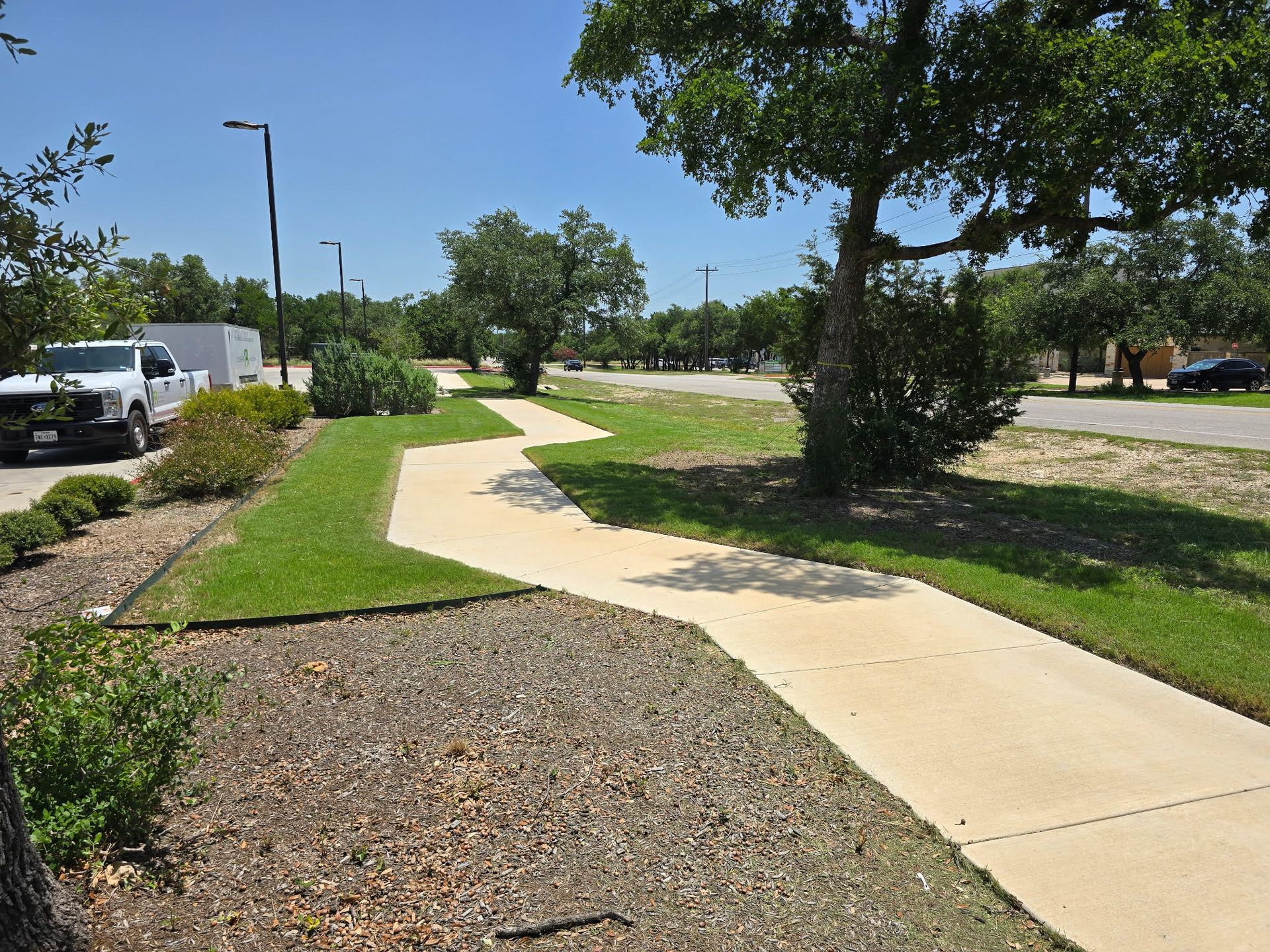 Concrete sidewalk with a zig-zag path in a park-like setting, bordered by grass and landscaping.